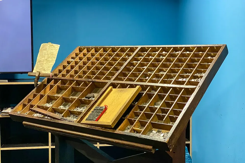A slanted wooden printer's type case on a stand, its many small compartments holding metal letters